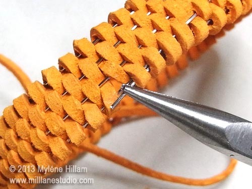 Feeding the end of the wire back into the suede lace weaving with chain nose pliers.