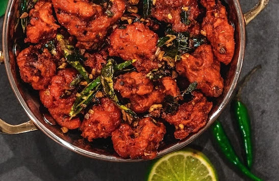 fried boneless chicken fillets in red color in deep pan along with lemon slice and lots of chilies