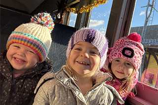 3 young girls smiling on a train.