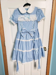 It is a blue and white old school Angelic Pretty dress. It has a peter pan collar, two corset things going down the front on the breast, it is tiered with white lace trim and it also has an odd trimming of white lace across the chest.