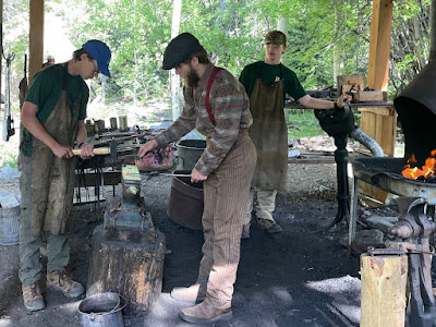 Two Scouts working with a staff member in period attire in a blacksmith shop.