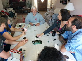 A group of people at a party sitting around a table playing The Resistance.