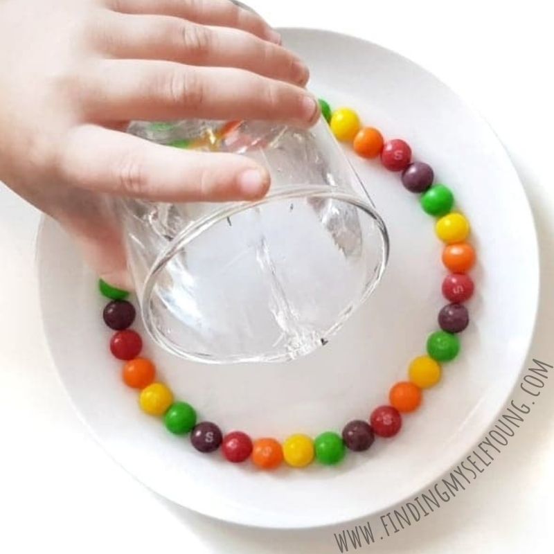 pouring water over skittles on a plate to create a rainbow