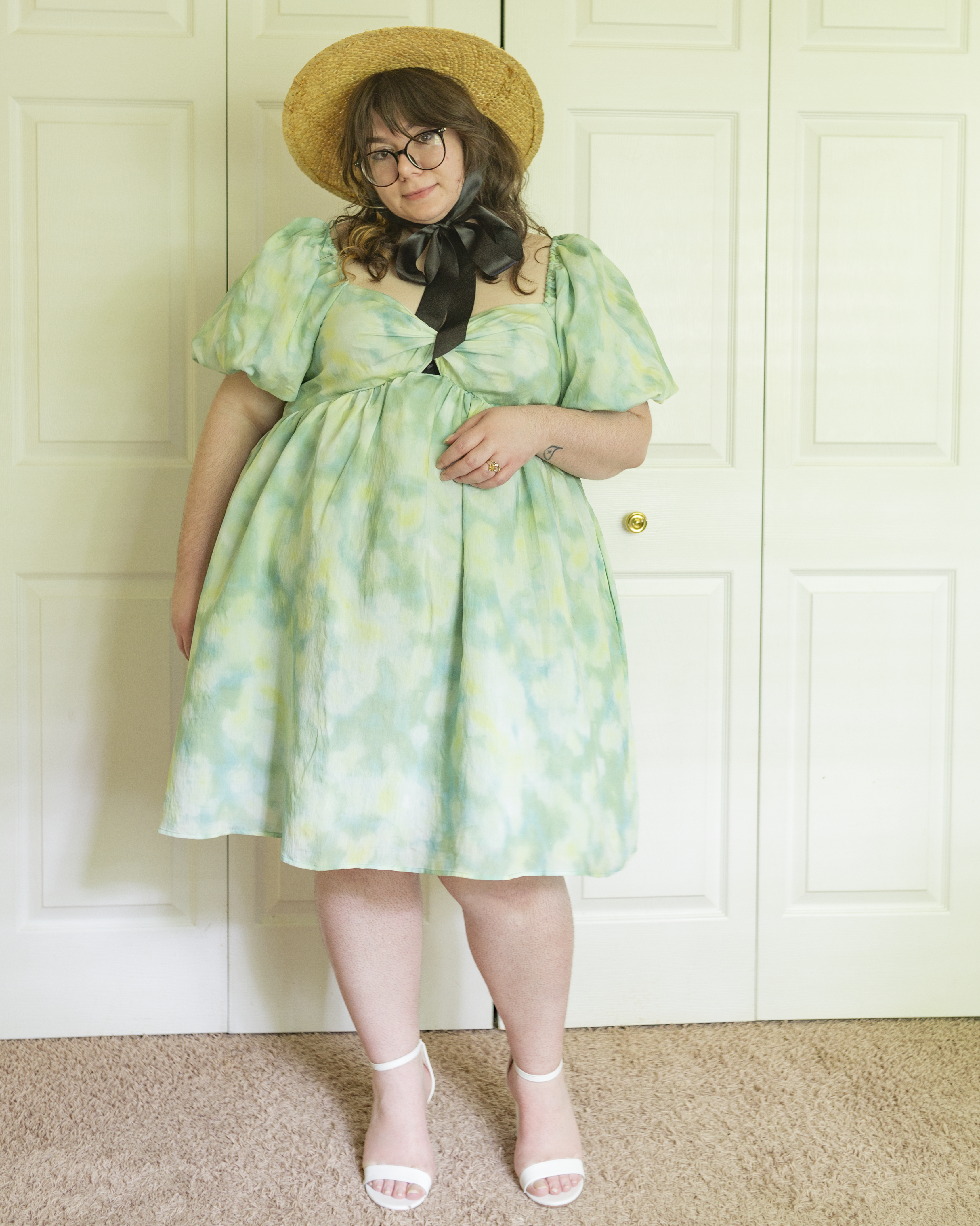 An outfit consisting of a star boater hat with a black silk ribbon that ties under the neck, a seafoam green and light blue tiedye puffy lsleeve empire waist mini dress and white ankle strap heeled sandals.