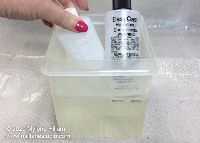 Resin and hardener bottles sitting in a container of warm water