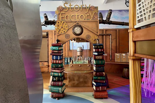 Sign saying Story Factory next to a seating area with paper and pencils for creativity at Discover