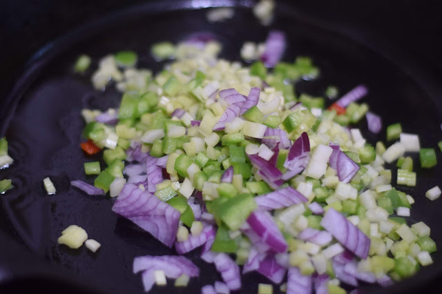 The green pepper, celery, and onion sautéing in a pan. 