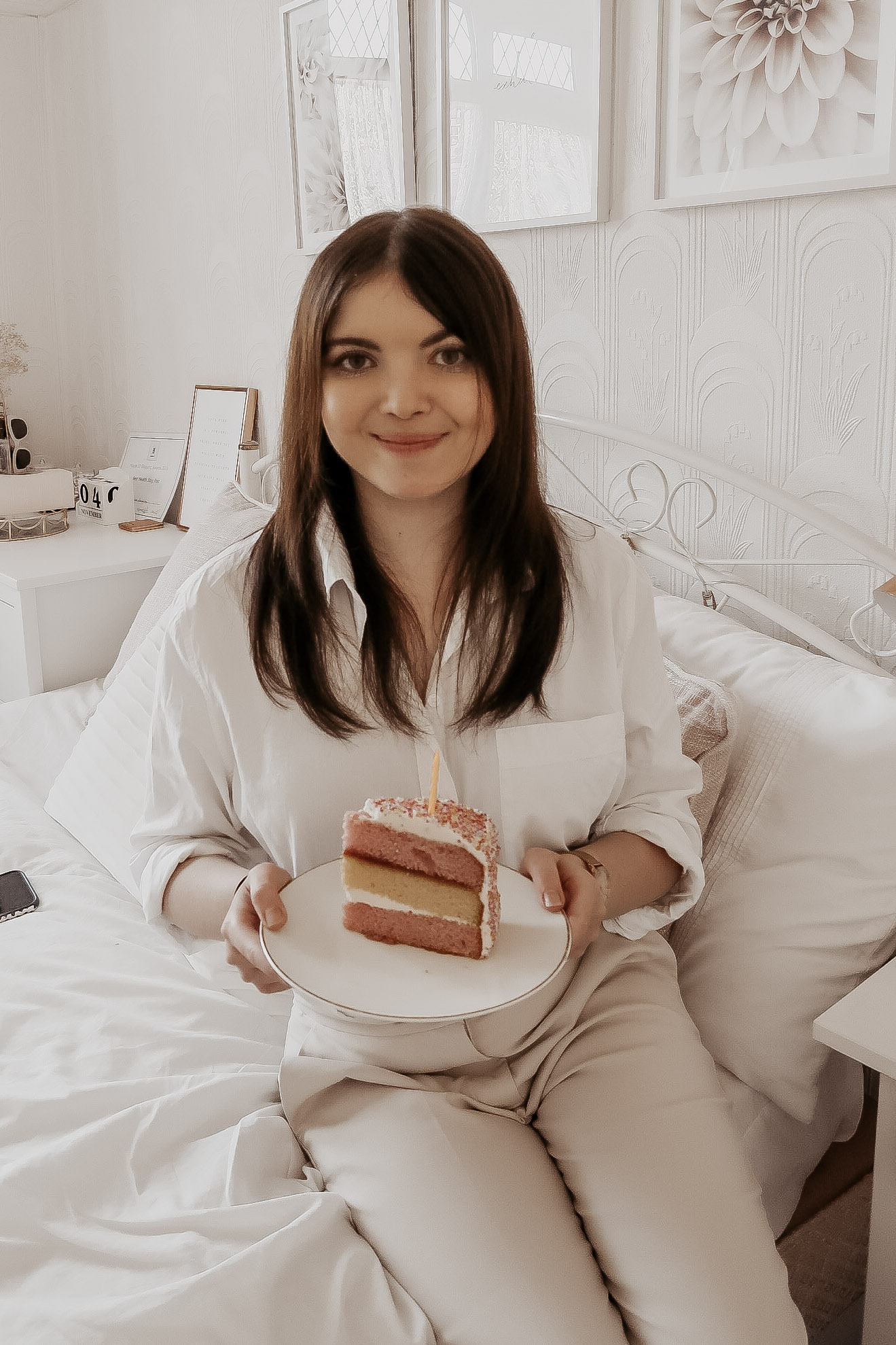 A woman sat on a bed holding a slice of cake.