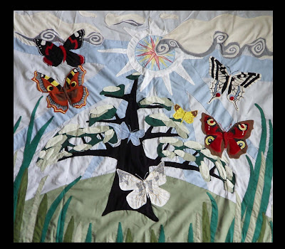 Machine appliqué with butterflies and tree. Foreground is long grass and background with large sunshine and clouds