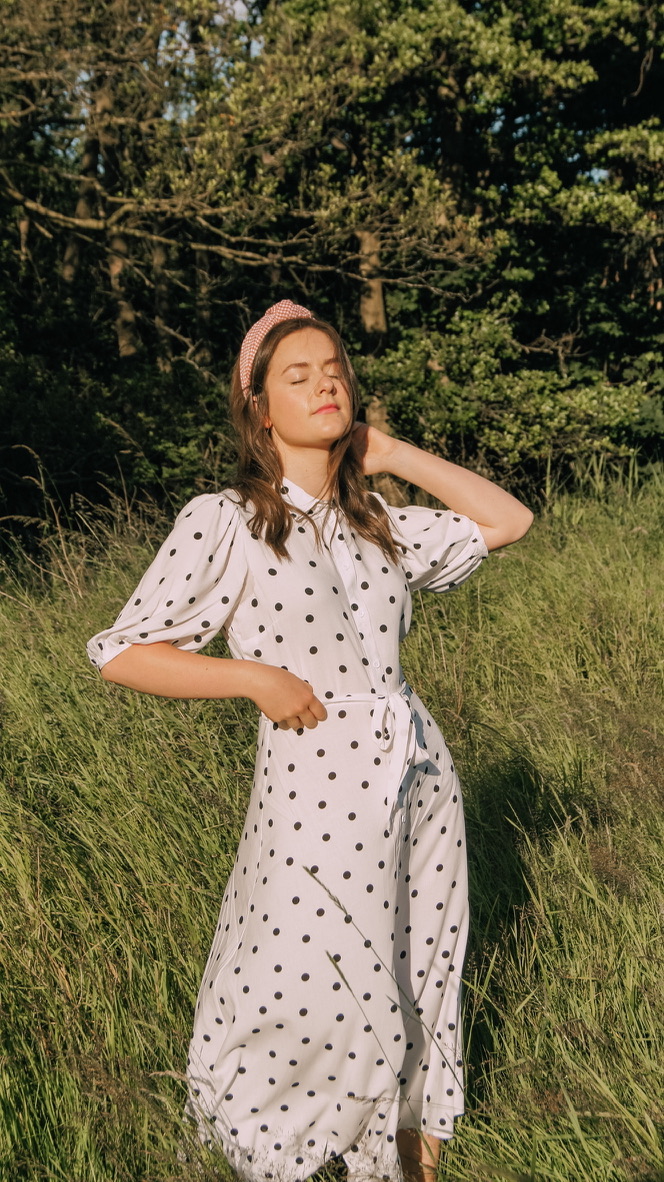 Brown haired girl in long grass wearing a white mid length dress