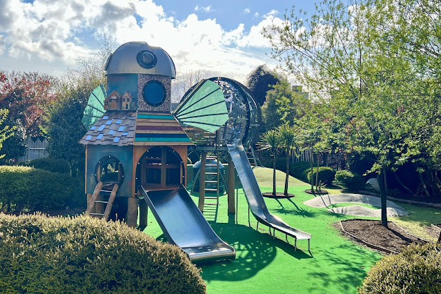 View from the entrance of the story garden showing the newest play structure with two slides and wings