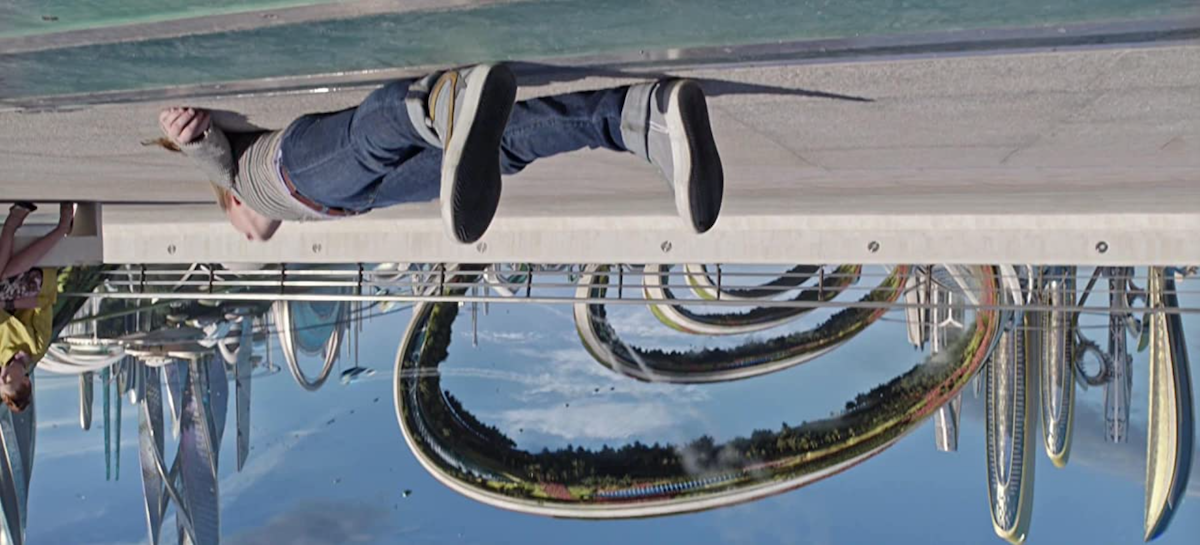 Britt Robertson's Casey lying flat on the ground in Tomorrowland, but the ground is above with the sky below