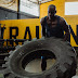 Man in blue tank top and shorts flipping a tire