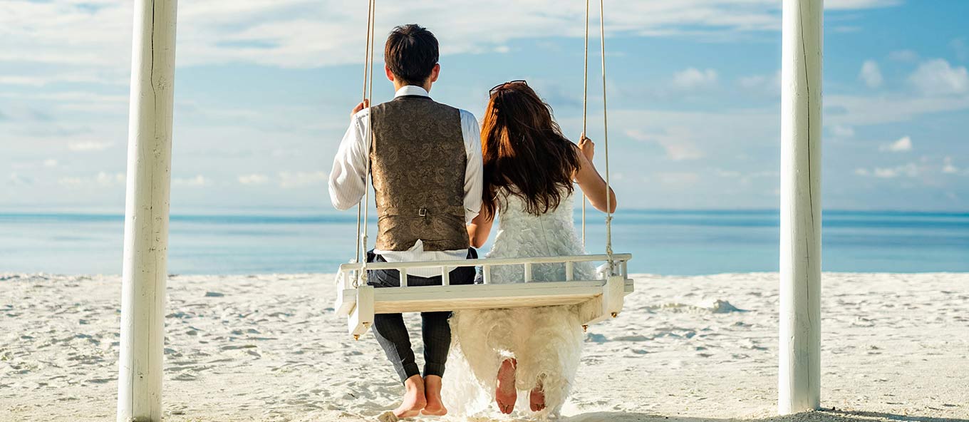 married couple holding hands on swing on the beach looking out into the ocean