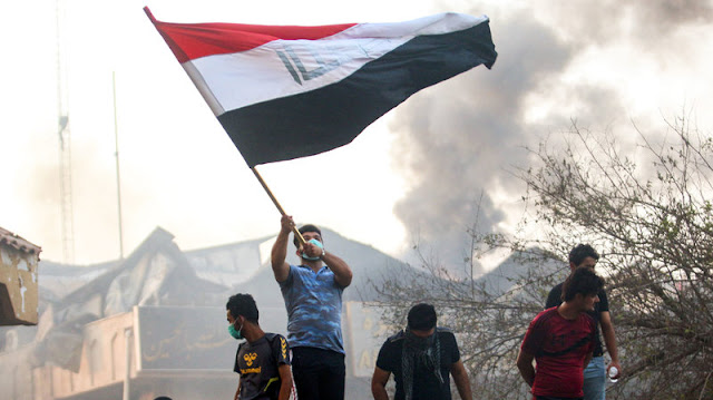 An Iraqi protester waves a national flag while demonstrating outside the burned-down local government headquarters in the southern city of Basra on Sept. 7, during demonstrations over problems including poor public services.