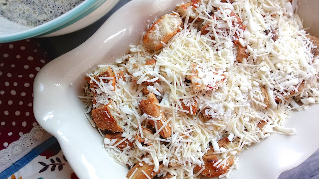 cheese covering torn pieces of pizza crust in a casserole dish next to a bowl of savory custard mix