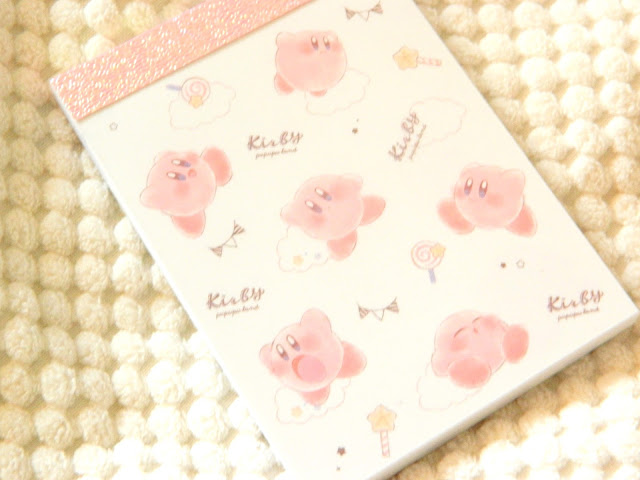 A photo showing the cover of a mini Kirby notepad, covered in cute kirby's, lollipops and wands