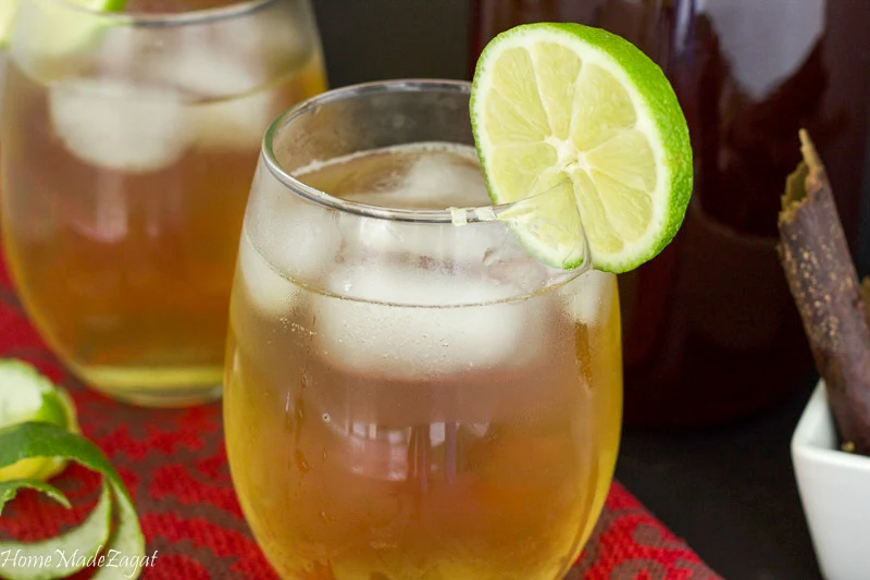 Close up of a glass of mauby with ice and lime rind