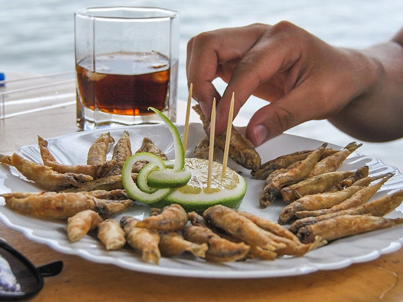 A plate of golden fried Sambaza fish served with a spicy dip and fresh lemon wedges.