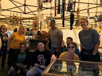 Lucas stands center next to a bear head and surrounded by smiling students, dream catchers, and wind chimes