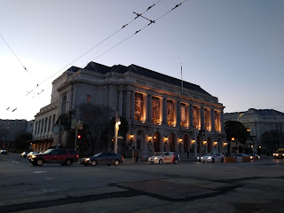 War Memorial Opera House at twilight. Photo shows a large neoclassical building with columns, a balcony, front steps, and a fly tower.