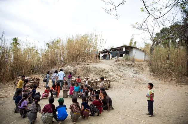 A imagem mostra um círculo de crianças em volta de um missionário numa tribo do interior africano.