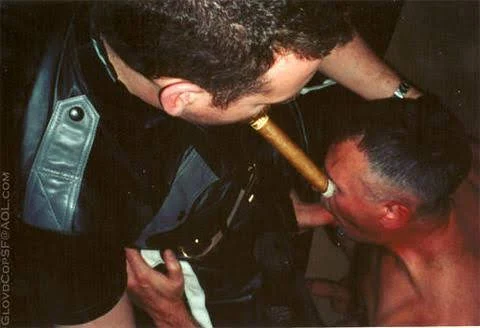 Glovedcop alpha leather master superior above a kneeling sexy muscle slave giving head while he puffs a cigar like an kinky pimp for adults over 18 years.