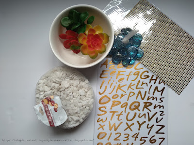 Craft materials such as faux succulents, ceramic bowl, craft rocks, and gold letter stickers