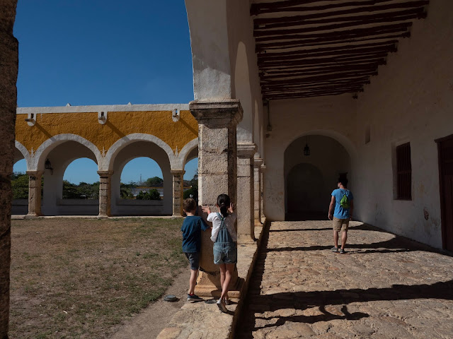 niños y hombre de espaldas paseando bajo los arcos del atrio del convento de San Bernardino en Izamal