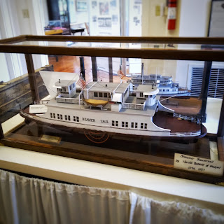 A model of a white ferry, about a foot long, inside a glass case.