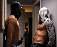 2 men wearing masks stand in a hallway in a sexually provocative pose