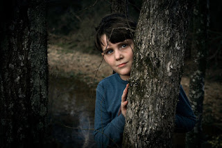 child in blue sweater standing behind a tree
