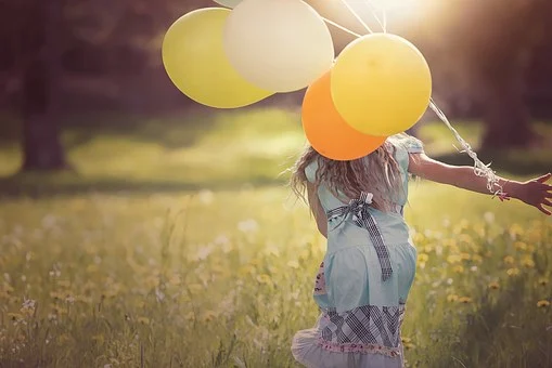 Una nena corre en un parque verde con muchos globos de colores en la mano