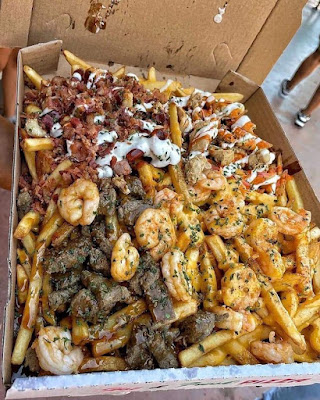 fries in a pizza box topped with bacon, chicken, steak, shrimp, various sauces and spices
