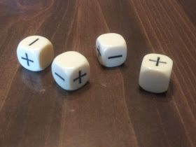 Four ivory-coloured plastic dice, each marked with pluses and minuses instead of numbers, on a glossy wooden surface.