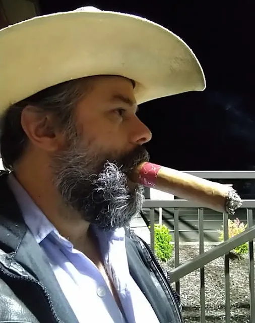 Side view of a salt and pepper bearded Cowboy wearing leather vest and smoking cigar