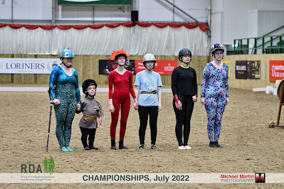 A group of six vaulters stand side by side at a competition before starting a team routine on the barrel horse. Three are dressed as dragons and three are dressed as Viking dragon riders (the theme is 'How to train your dragon'!) They are looking up, some are smiling and some look determined.