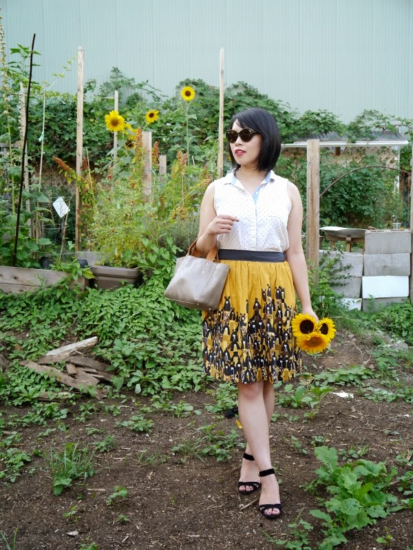 Sleeveless swiss dot blouse, patterned yellow skirt, black suede sandals, cat-eye shades