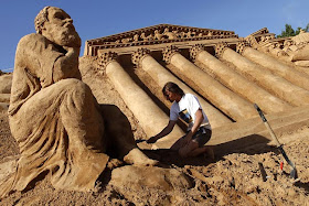 sculptor works on a sand sculpture of The Thinker