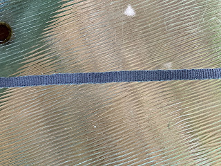 a close up of a narrow, dark grey woven band. Small pops of the lighter grey weft can be seen on the selvedges. End ID.