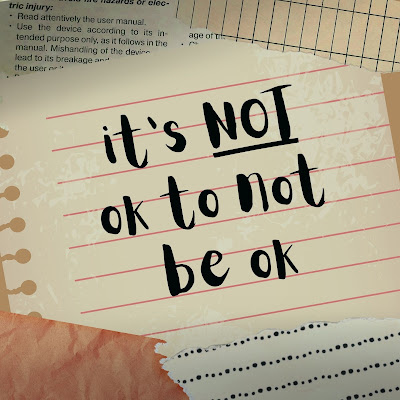 The words, "It's NOT ok to not be ok," appear in a handwritten font on a piece of lined notebook paper surround by other pieces of ripped scrap paper.