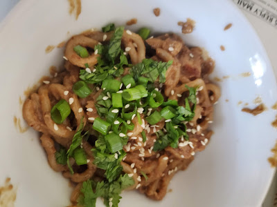 A pile of noodles with light brown sauce, green onion slices, and sesame seeds