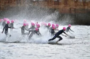 Triatletas com touca rosa se jogando na água