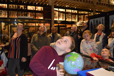 A group of people look upwards as they are looking to the top of the totem pole to estimate its height