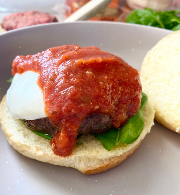 Close up of burger on a bun with fresh mozzarella cheese and marinara sauce.