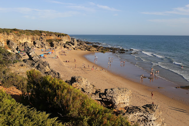 Gran playa de arena con forma de herradura con gente, rodeada de acantilados rocosos.