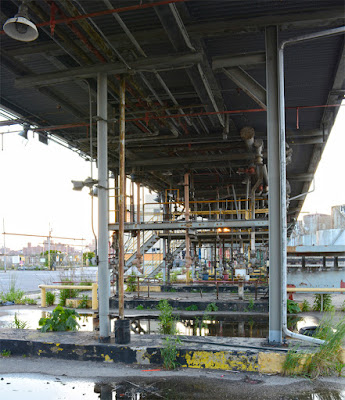 Oil works pipes and truck stalls with weeds growing in pavement cracks