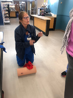 Nurse Nora kneeling beside a foam model, in which a red t-shirt is packed into a fake wound.