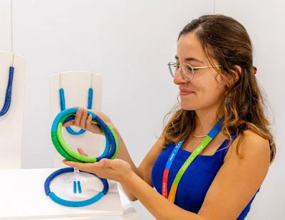 smiling young woman holding bright, circular necklace composed of green and blue discs.