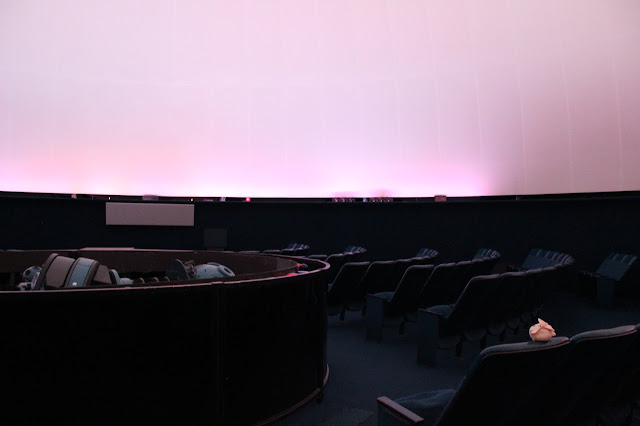 In a planetarium with a big 70' diameter dome sits many blue seats that face the center.  In the center is a Zeiss Universarium Mark VI projector which looks like a dumbbell. On one of the closest chairs sits Little Star (a smiling yellow star) looking up.